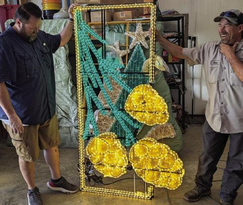 Successful testing the lights brings grins of approval as town workmen put together the large lamp post ornaments.That’s Randal Wilson, at left, and Mike McCune who are adding to the downtown holiday spirit.